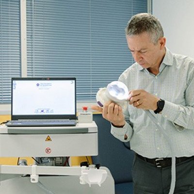 A man stands looking at an ultrasound machine in a hospital room or clinical setting. 